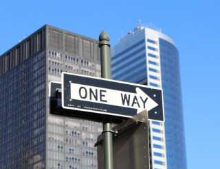 A one way street sign with skyscrapers in the background.