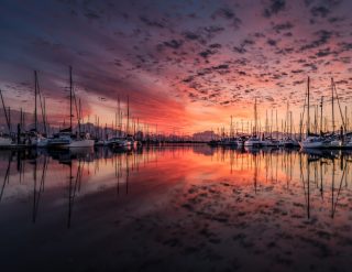 A harbour of yachts with a vibrant pink sunset in the sky and reflected in the water.