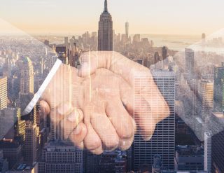 Two hands in a handshake superimposed over a photo of a city of skyscrapers.