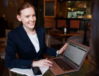 A professional-looking lady is holding a laptop with smile on her face.